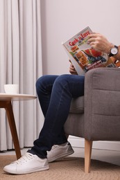 Photo of Man reading magazine in armchair at home, closeup