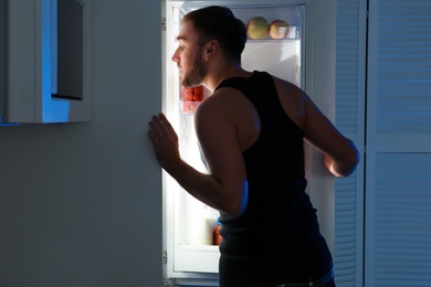 Photo of Man taking products out of refrigerator in kitchen at night