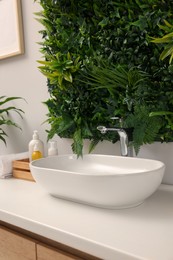 Green artificial plants, vessel sink and different personal care products in bathroom