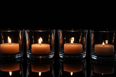 Photo of Wax candles burning on table in darkness, closeup