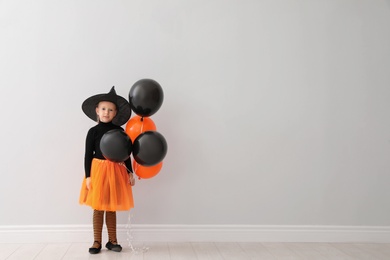 Photo of Cute little girl with balloons wearing Halloween costume near light wall. Space for text