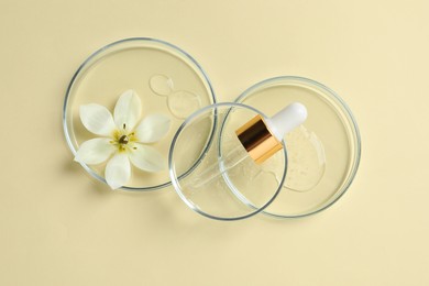 Photo of Petri dishes with samples of cosmetic oil, pipette and beautiful flower on beige background, flat lay