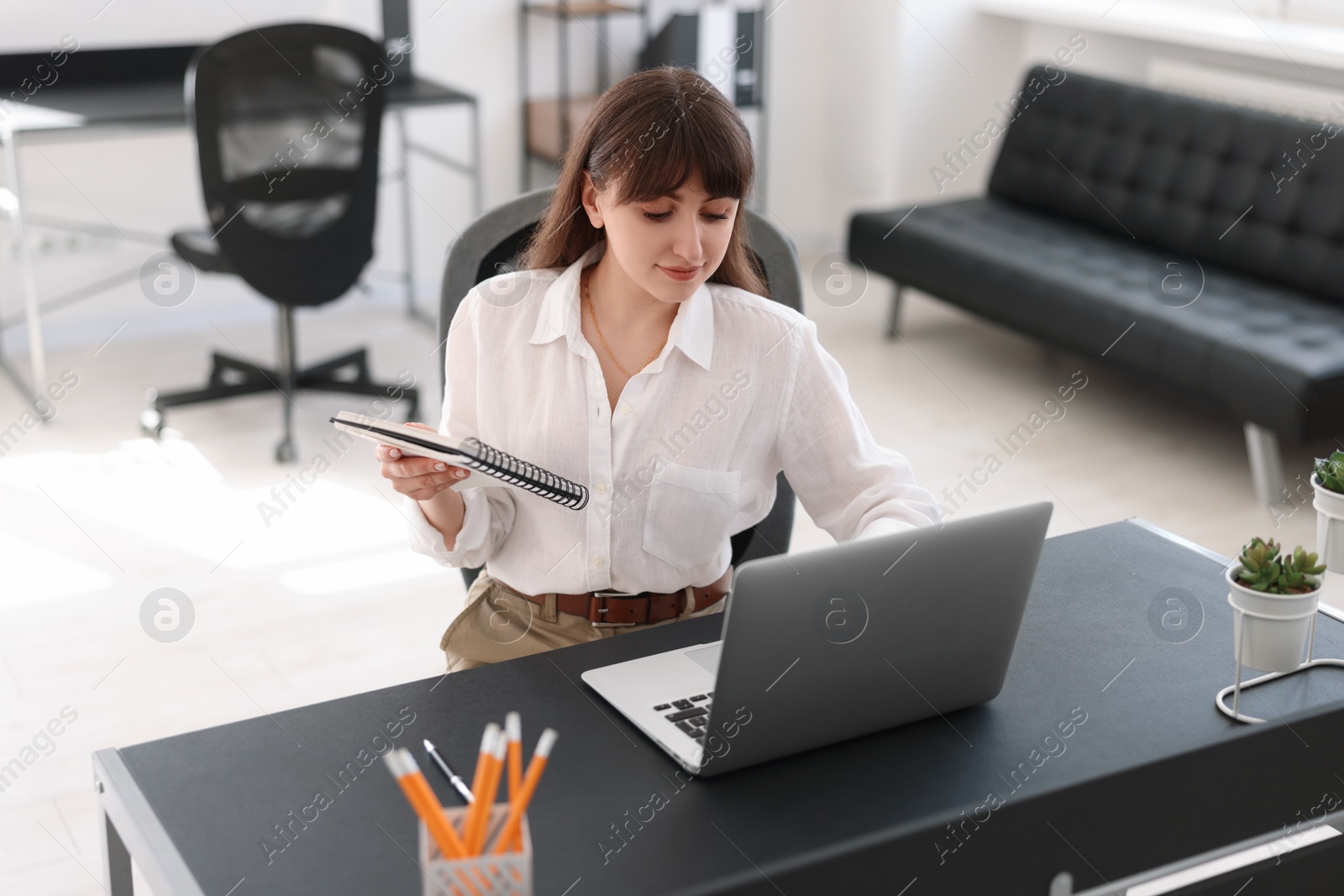 Photo of Woman with notebook watching webinar at table in office