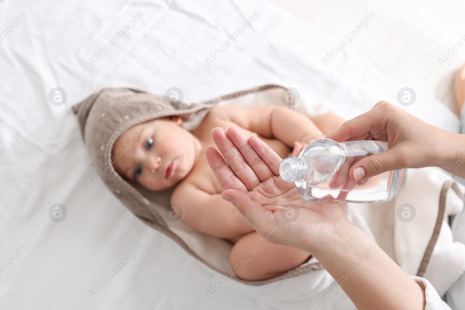 Photo of Mother with bottle of massage oil near baby on bed, closeup