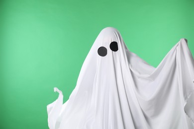 Photo of Creepy ghost. Person covered with white sheet on green background, space for text