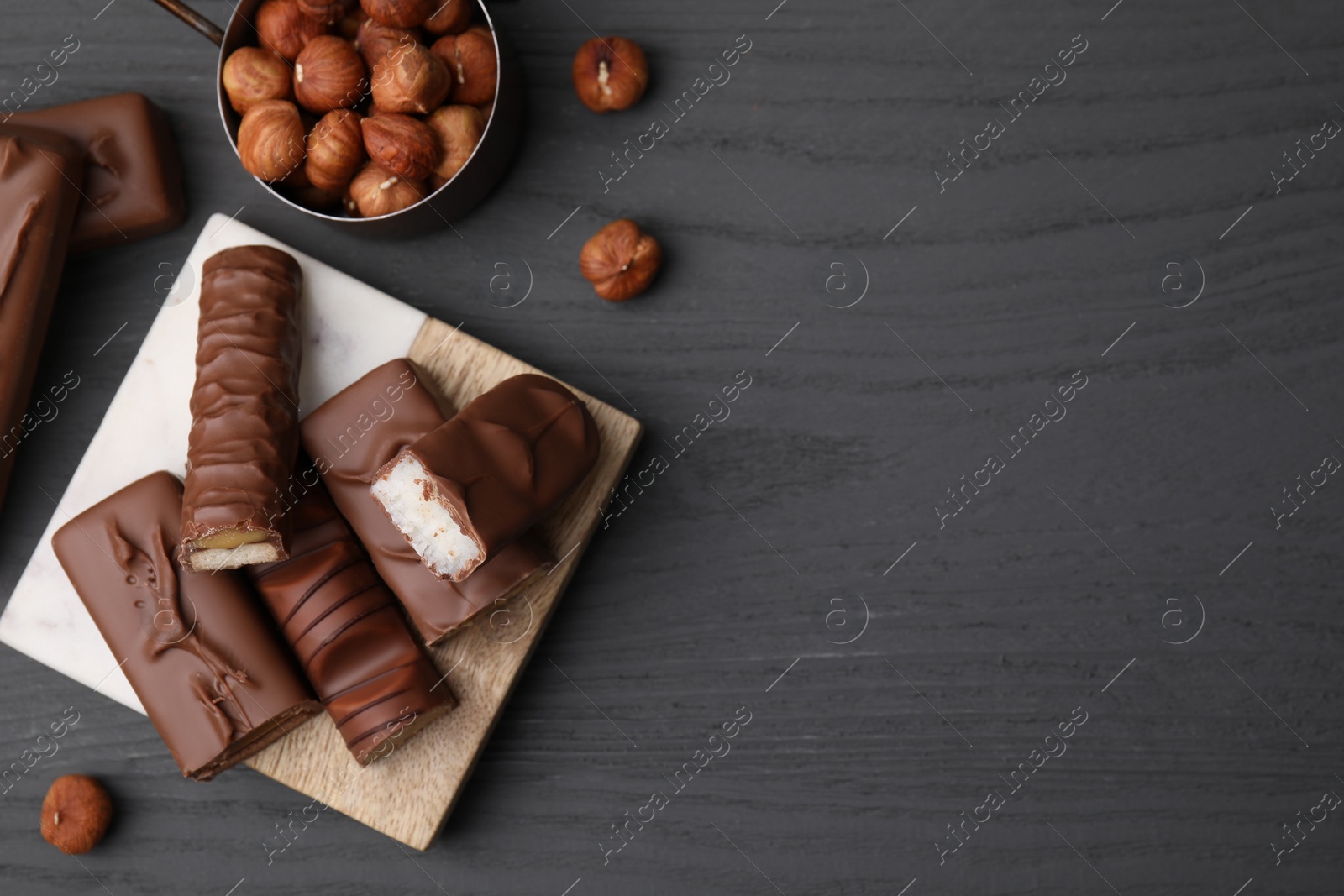 Photo of Pieces of different tasty chocolate bars and hazelnuts on grey wooden table, flat lay. Space for text