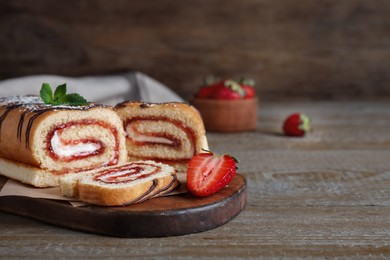 Tasty cake roll with strawberry jam and cream on wooden table, space for text