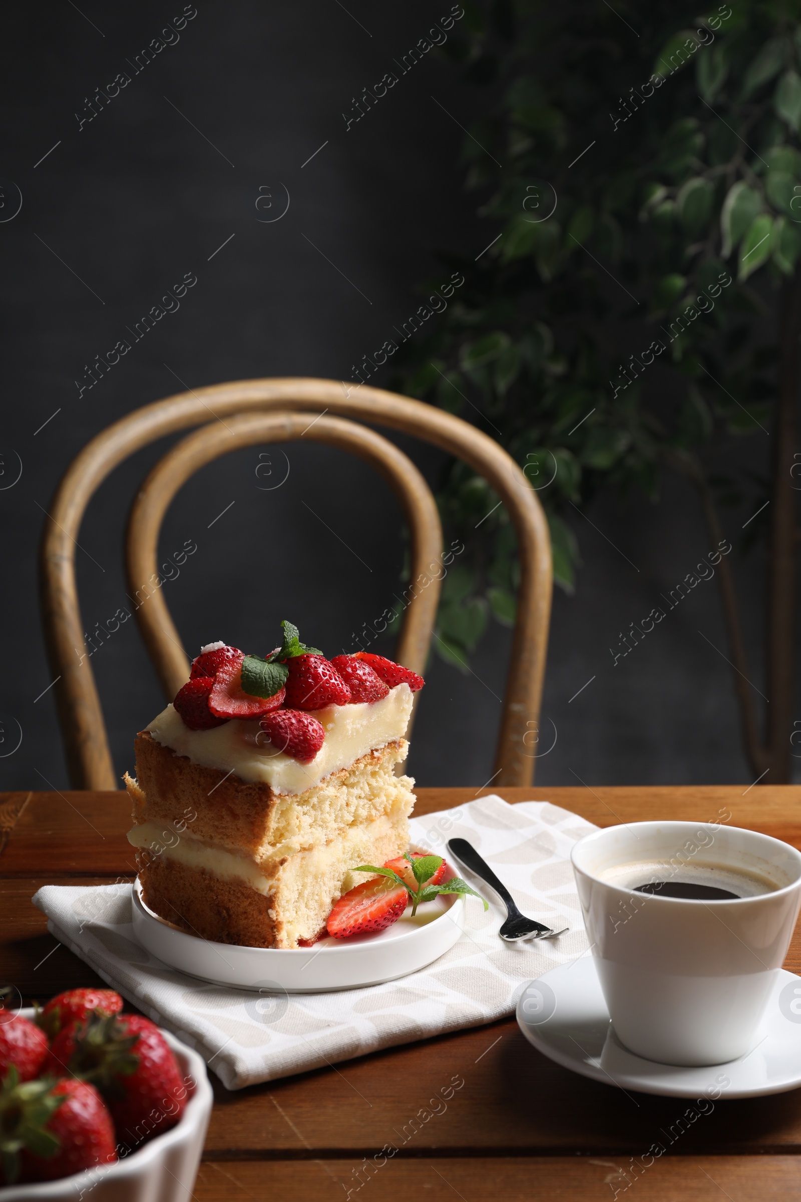 Photo of Piece of tasty cake with fresh strawberries, mint and cup of tea on wooden table