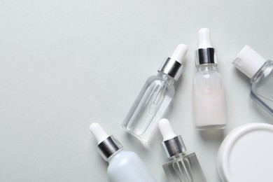 Many bottles of cosmetic serum on light grey background, flat lay. Space for text