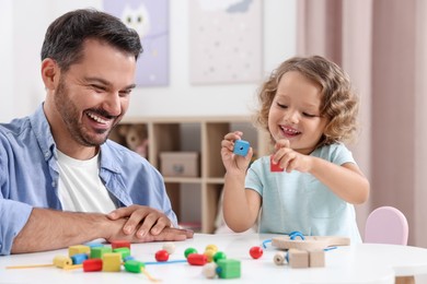 Photo of Motor skills development. Father and daughter playing with wooden pieces at table indoors