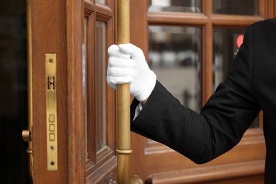 Photo of Butler in elegant suit and white gloves opening hotel door, closeup
