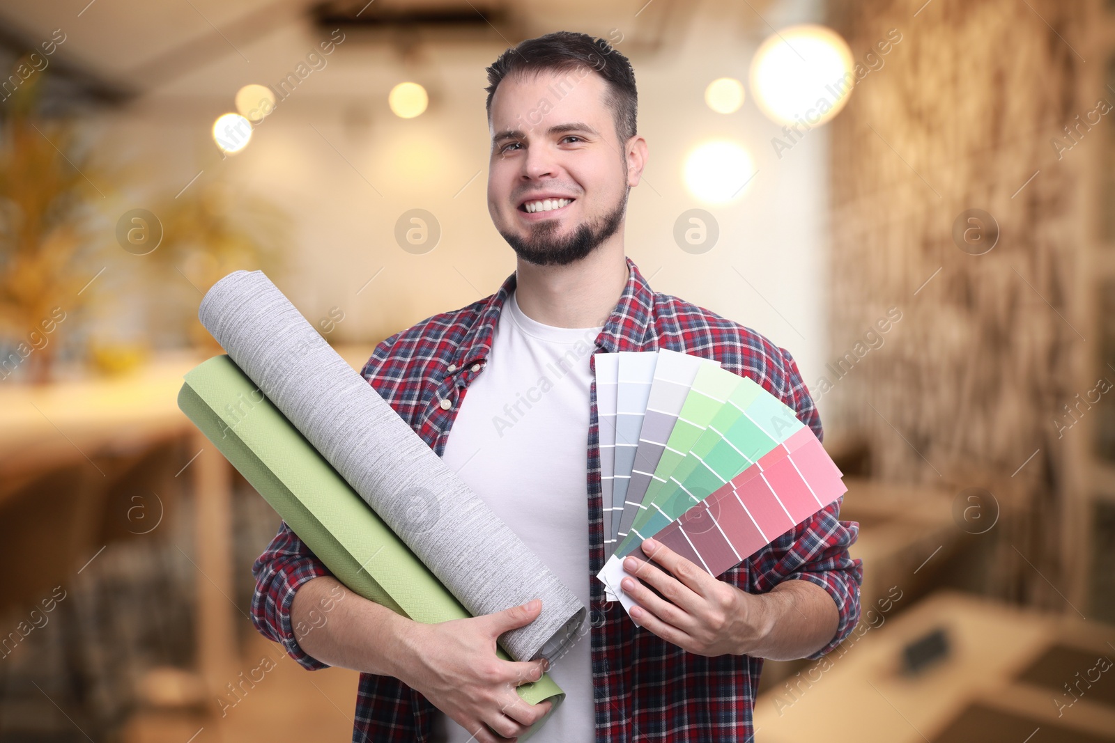 Image of Man with wallpaper rolls and color selection chart on blurred background