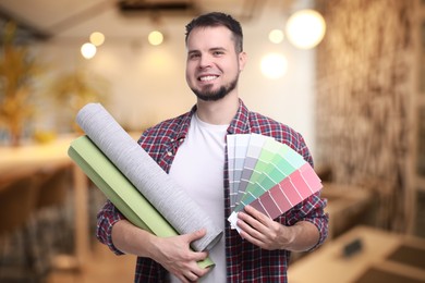 Man with wallpaper rolls and color selection chart on blurred background