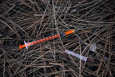 Photo of Disposable syringe with needle on heap of dry branches