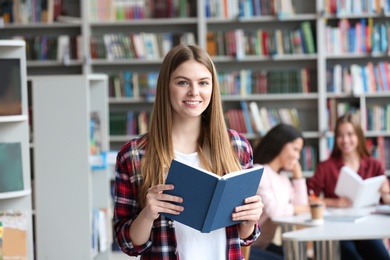 Young pretty woman with book in library