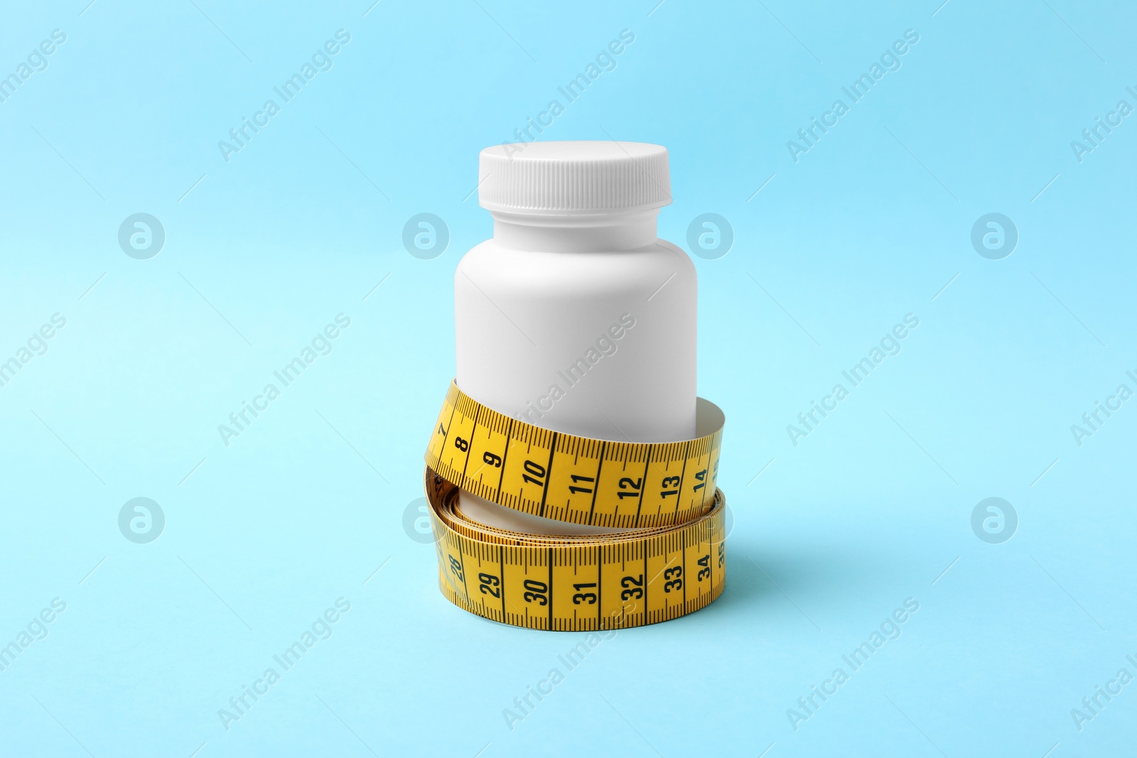 Photo of Bottle of weight loss pills with measuring tape on color background