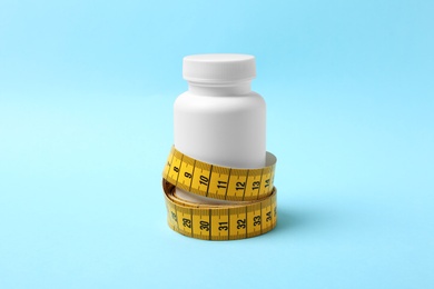 Photo of Bottle of weight loss pills with measuring tape on color background