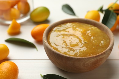 Delicious kumquat jam in bowl and fresh fruits on white wooden table, space for text