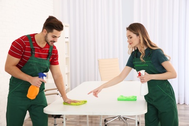 Photo of Professional janitors cleaning table in office. Hired help
