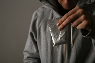 Photo of Drug dealer holding bag with cocaine on dark background, closeup. Space for text