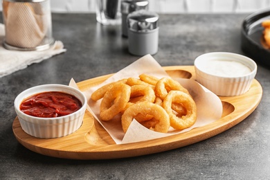 Photo of Wooden board with tasty onion rings and sauces on table, closeup