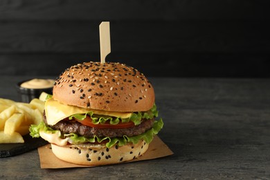 Photo of Burger with delicious patty and french fries on gray table against dark background, space for text