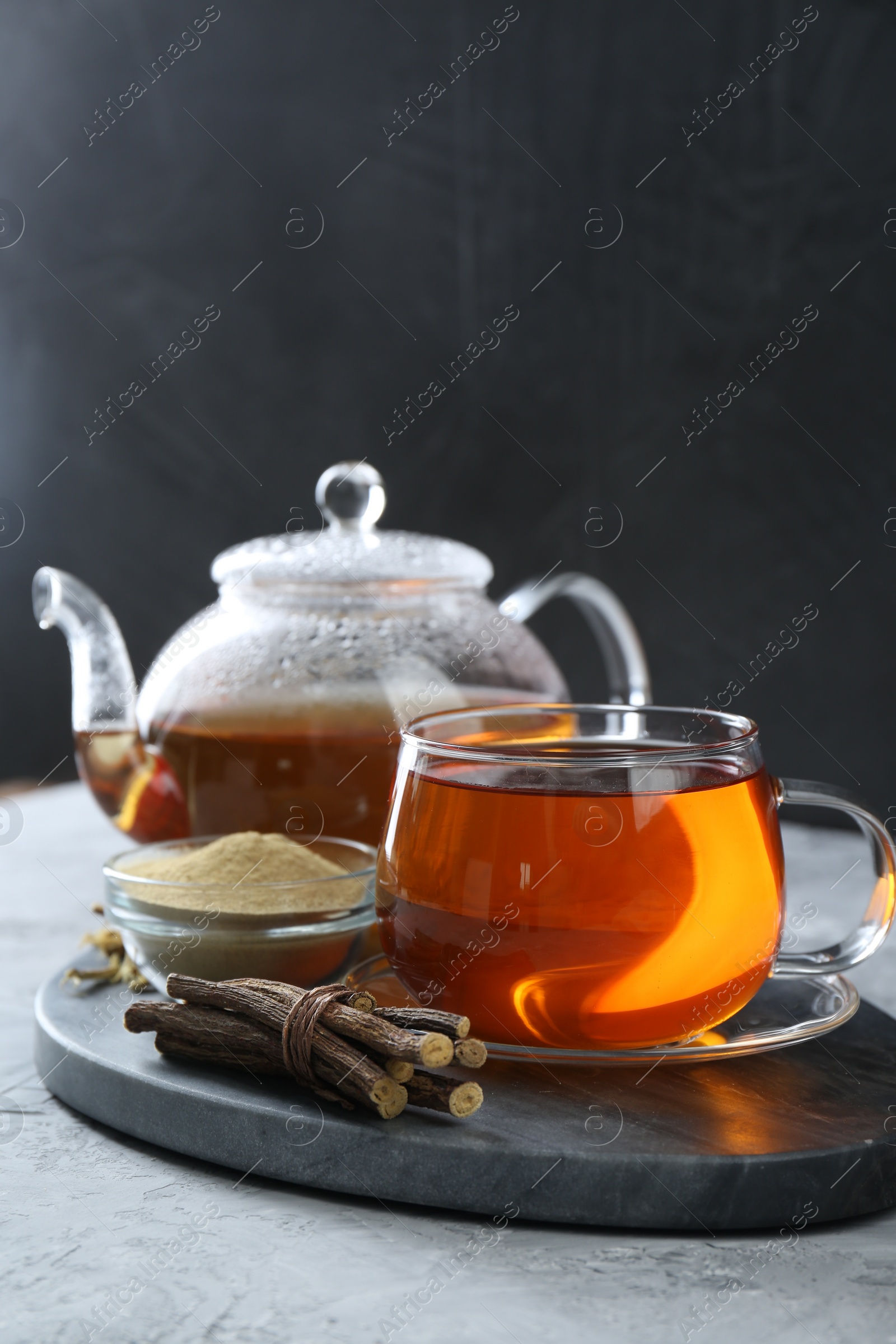 Photo of Aromatic licorice tea, dried sticks of licorice root and powder on light gray textured table, space for text