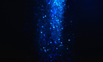 Shiny blue glitter falling down on black background. Bokeh effect