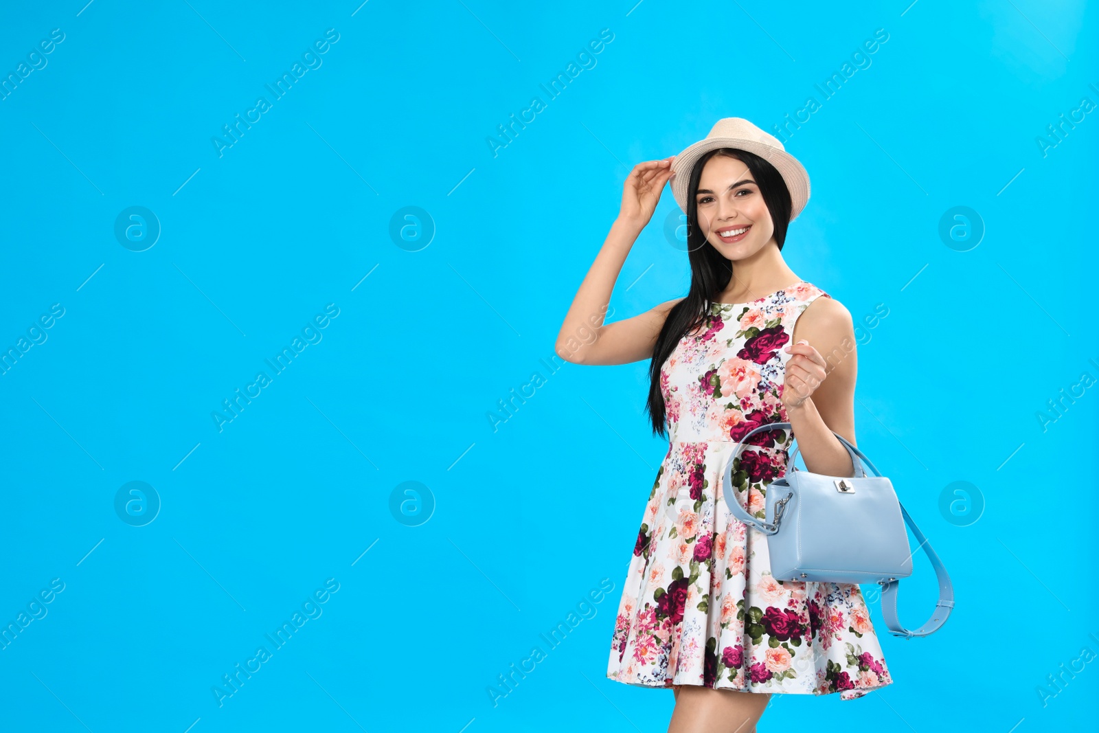 Photo of Young woman wearing floral print dress with stylish handbag on light blue background. Space for text