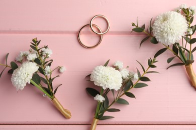 Photo of Small stylish boutonnieres and rings on pink wooden table, flat lay
