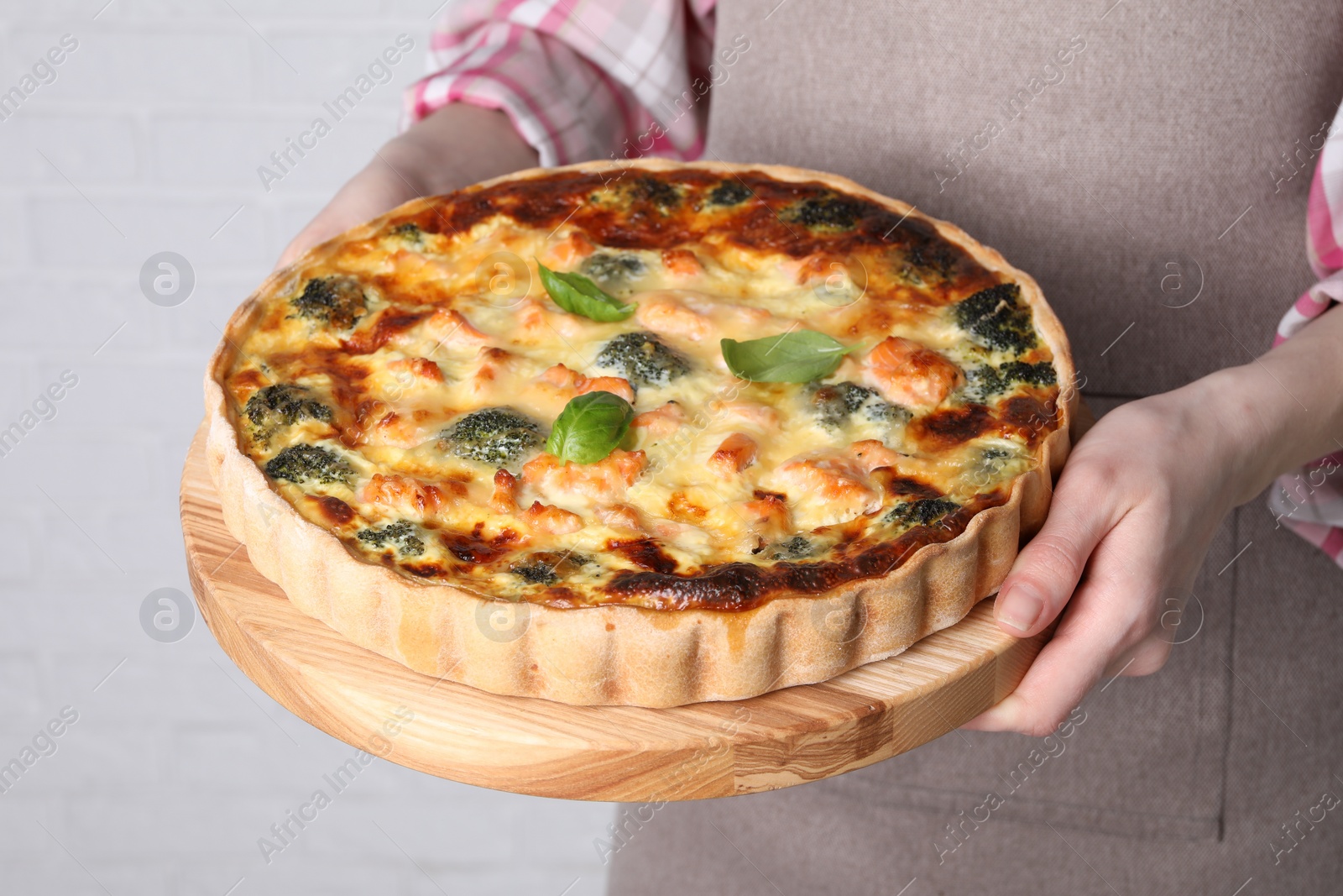 Photo of Woman holding delicious homemade quiche with salmon and broccoli on light background, closeup