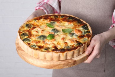 Woman holding delicious homemade quiche with salmon and broccoli on light background, closeup