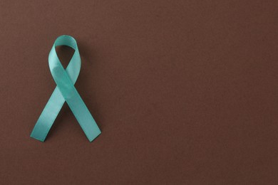 Turquoise awareness ribbon on brown background, top view. Space for text