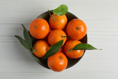 Photo of Delicious tangerines with green leaves in bowl on white wooden table, top view