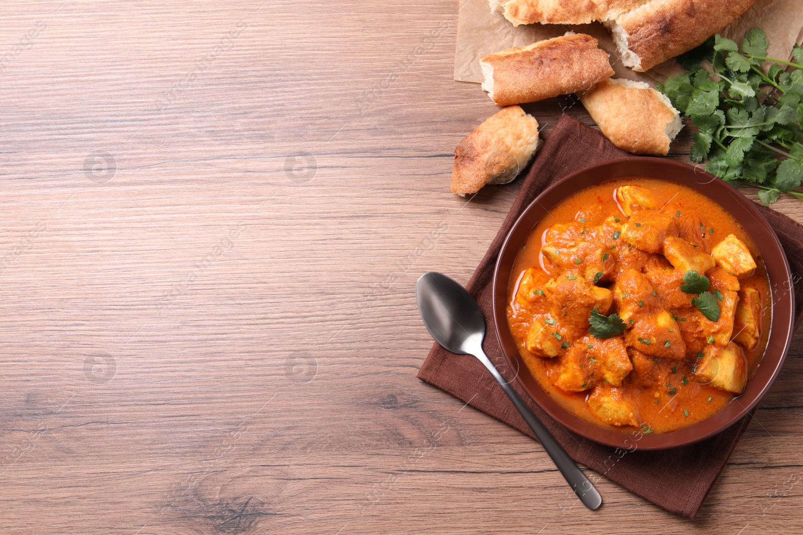 Photo of Bowl of delicious chicken curry on wooden table, flat lay. Space for text