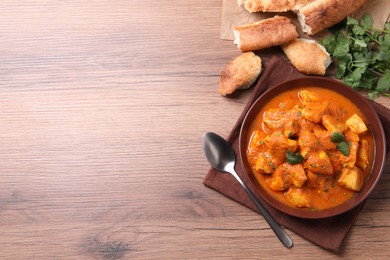 Bowl of delicious chicken curry on wooden table, flat lay. Space for text