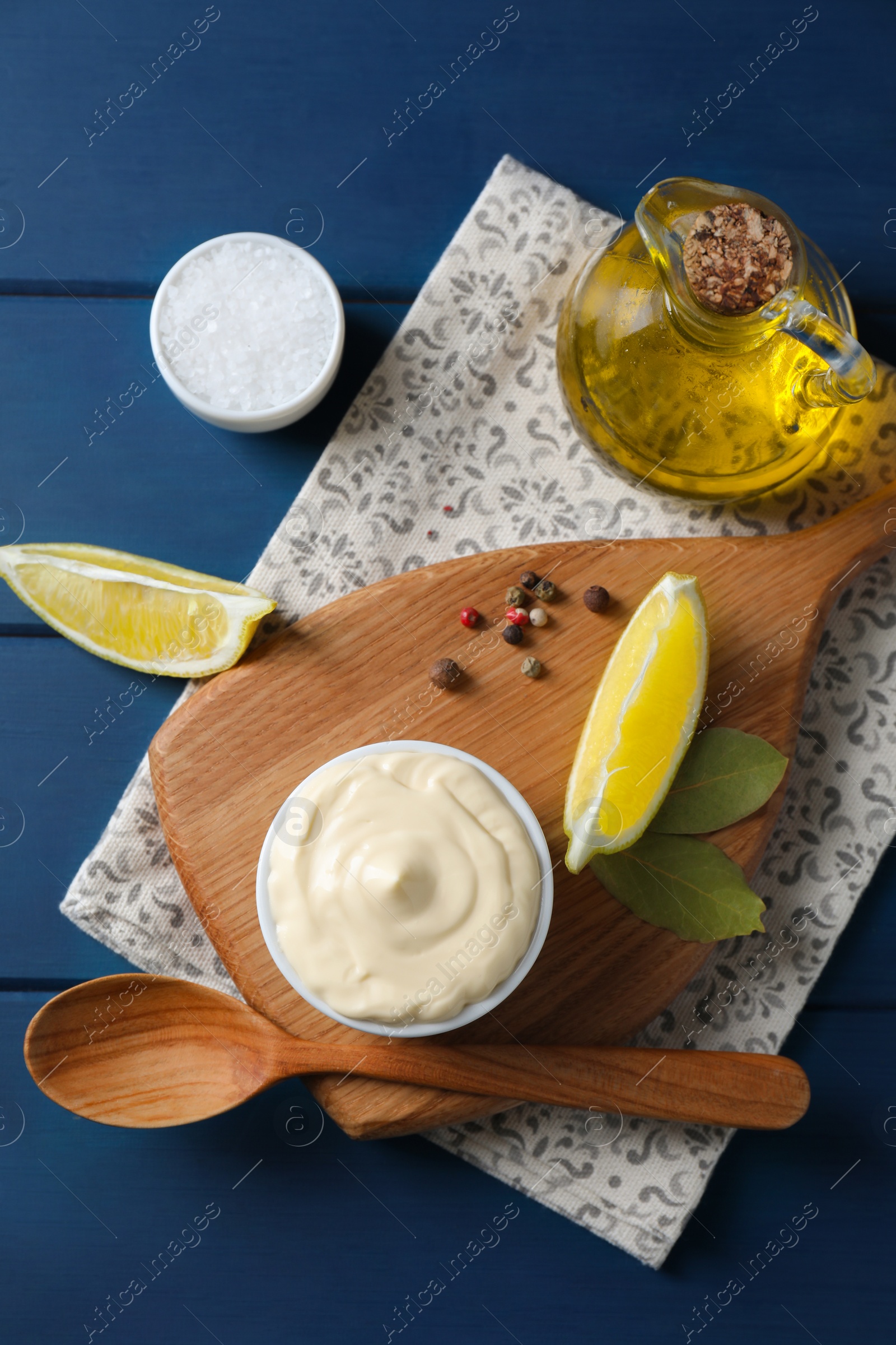 Photo of Tasty mayonnaise in bowl, products and spoon on blue wooden table, flat lay