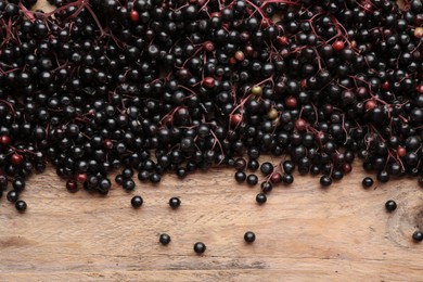 Photo of Black elderberries (Sambucus) on wooden table, flat lay. Space for text