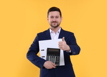Photo of Happy accountant with calculator and folder showing thumb up on yellow background