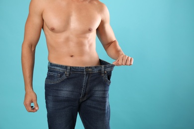 Photo of Young man with slim body in old big size jeans on light blue background, closeup view. Space for text