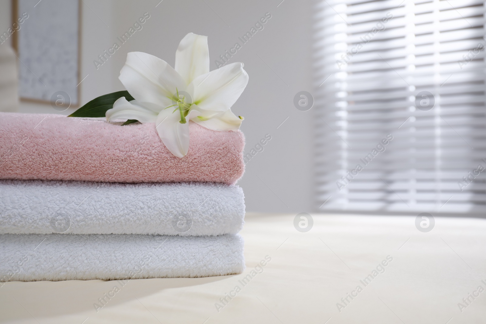 Photo of Stack of clean towels and flower on bed indoors, closeup. Space for text