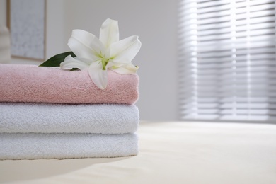 Stack of clean towels and flower on bed indoors, closeup. Space for text