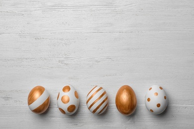Photo of Set of traditional Easter eggs decorated with golden paint on wooden background, top view. Space for text