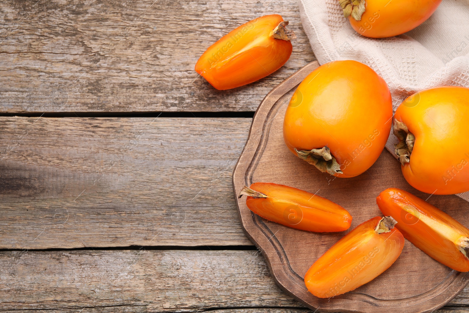 Photo of Whole and cut delicious ripe persimmons on wooden table, top view. Space for text