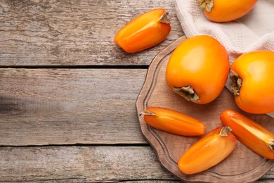 Whole and cut delicious ripe persimmons on wooden table, top view. Space for text