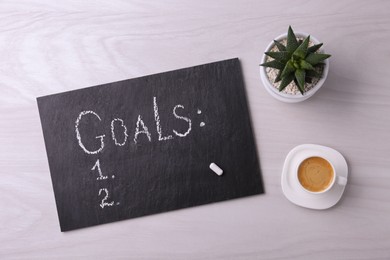 Photo of Slate board with word Goals, numbering, houseplant and cup of coffee on white wooden table, flat lay. Planning concept