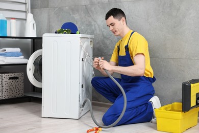 Photo of Young plumber examining drain hose of washing machine in bathroom