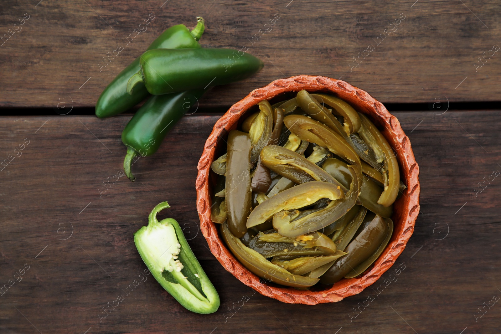 Photo of Fresh and pickled green jalapeno peppers on wooden table, flat lay