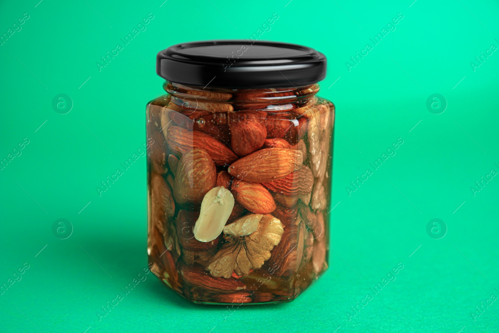Photo of Jar with different tasty nuts and honey on green background