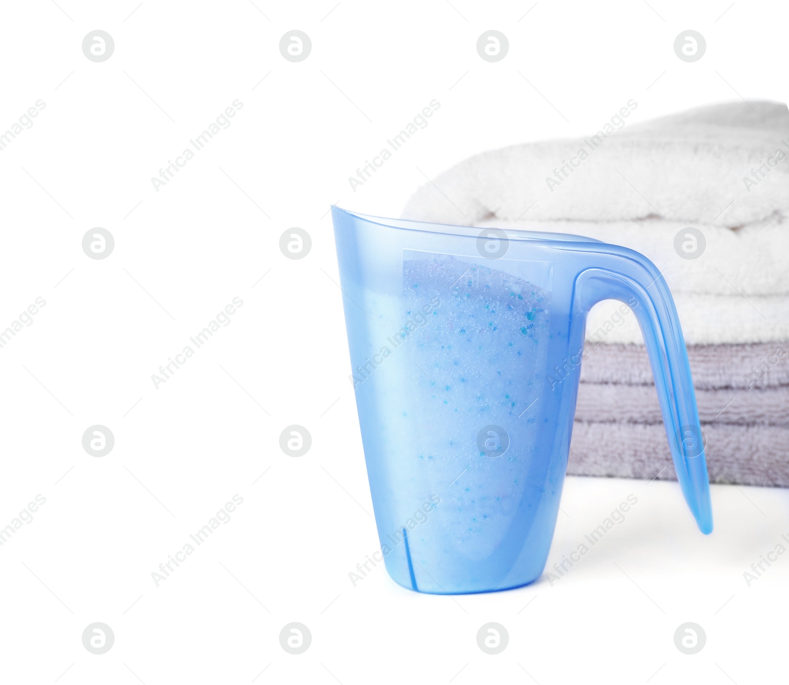 Photo of Laundry detergent in plastic measuring cup and towels on white background